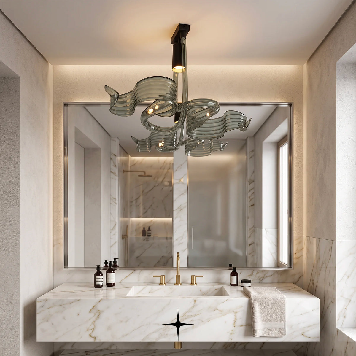 A modern bathroom interior featuring a sculptural glass chandelier with a black central stem and warm glowing bulbs, mounted above a marble vanity with a large mirror.