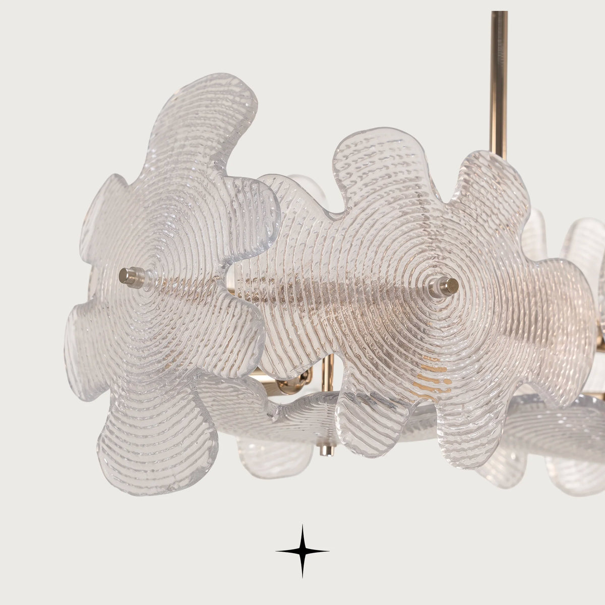 A close-up of a modern nika chandelier featuring textured, translucent clear glass flower-shaped shades with a brushed gold metal rod and small gold hardware, set against a solid off-white background.