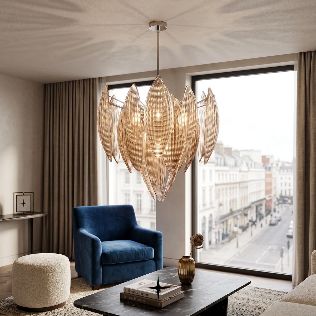 A Lotus luxury circular chandelier featuring amber crystal lotus glass leaves and gold core frame chandelier with leaf-like textured shades hangs in a stylishly furnished living room with a blue armchair, coffee table, and large windows overlooking a city street.