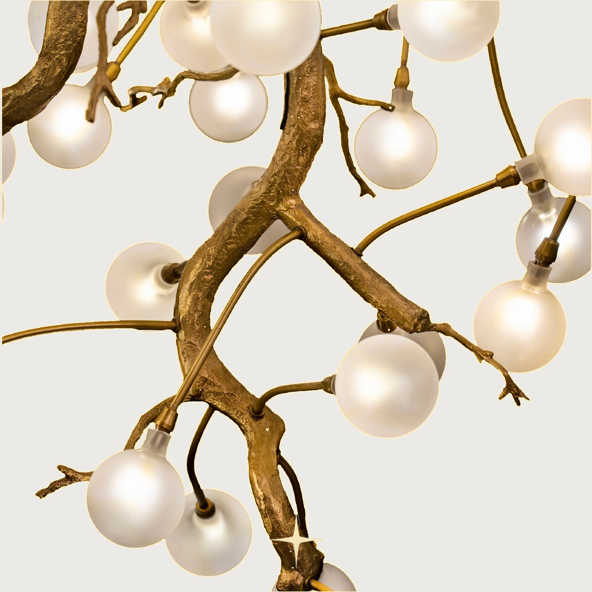 Front view of Romantica organic brass branch chandelier with white glowing bulbs on light grey backdrop