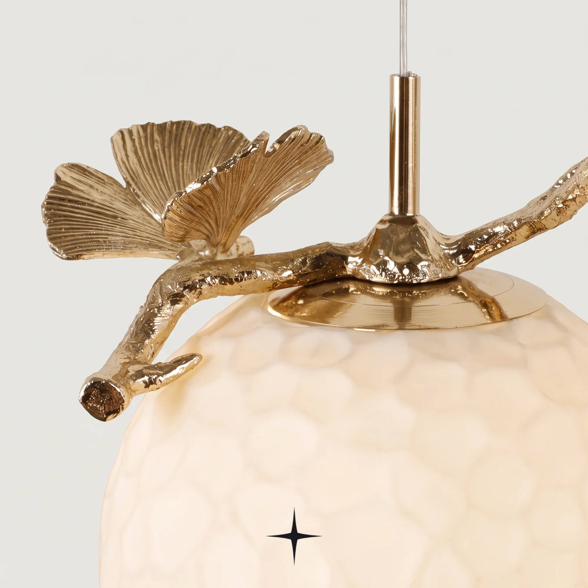 Close up detail of gold ginkgo leaf ornament attached to the textured sphere glass shade of Zara pendant light