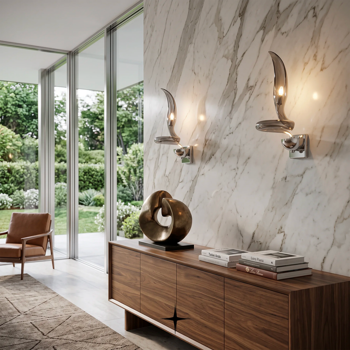 Two modern curved wall sconces with polished silver metal mounts and warm glowing bulbs, mounted on a white marble wall above a wooden console in a stylishly decorated interior.