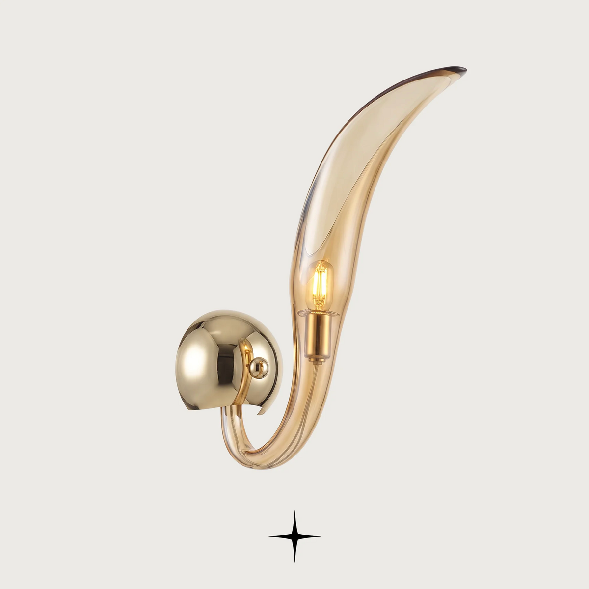 A modern wall-mounted light fixture with a curved, leaf-like transparent smoked glass shade and a polished gold-toned metal mount, shown against a light gray background.