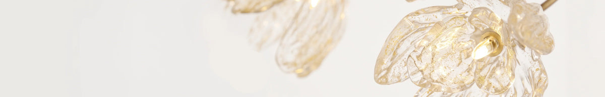 A close-up of a translucent glass flower-shaped pendant light with a warm glowing bulb inside, set against a clean white background.