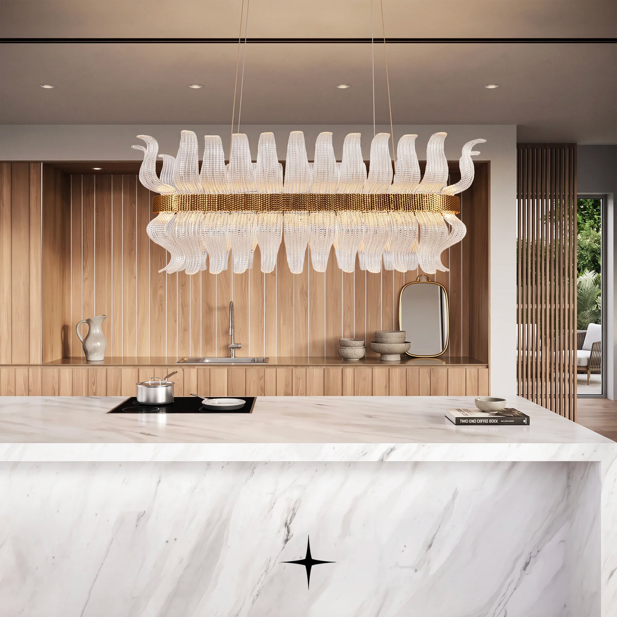 A modern kitchen island with a white marble countertop and backsplash, featuring a large, Linear Helena chandelier featuring handcrafted Murano glass leaves and gold frame. The background includes warm wood paneling, a built-in sink, and decorative ceramic vessels.